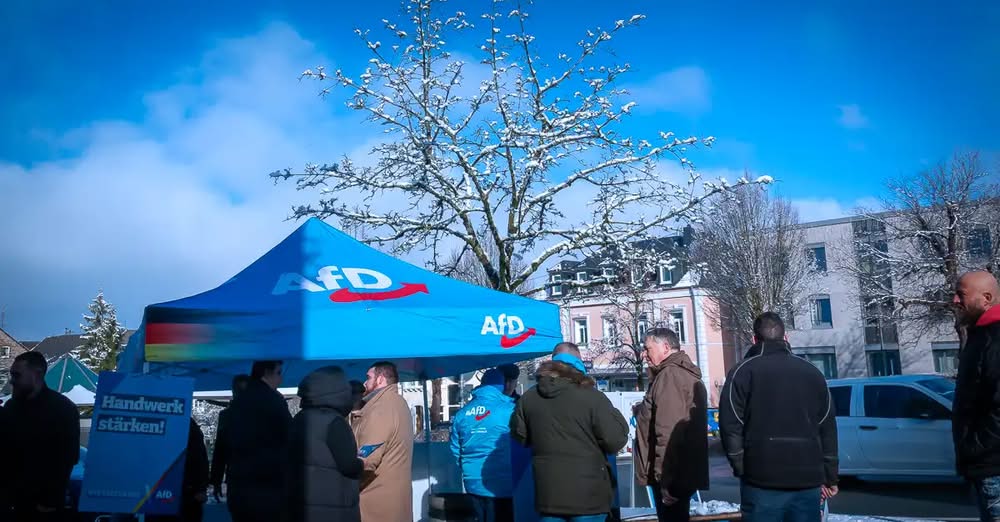 AfD Infostand unter einem blauen Pavillon auf einem Marktplatz, mehrere Bürger stehen im Gespräch mit Parteimitgliedern an einem Informationsstand der AfD Westerwald.
